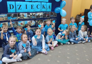 Dzieci pozują do zdjęcia w niebieskich strojach, w rękach trzymają wycięte z papieru serca